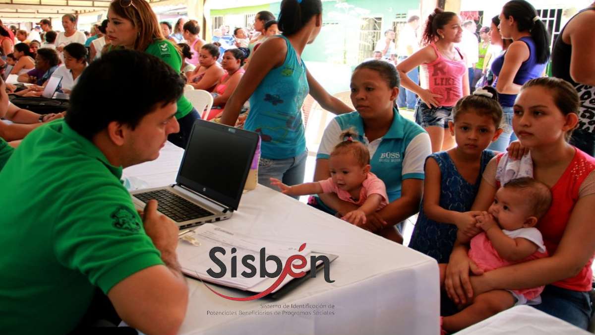 Puntaje Sisbén 2024-MP Noticias, hombre de camisa verde con computador prestando información a grupo de mujeres con niños en bazos
